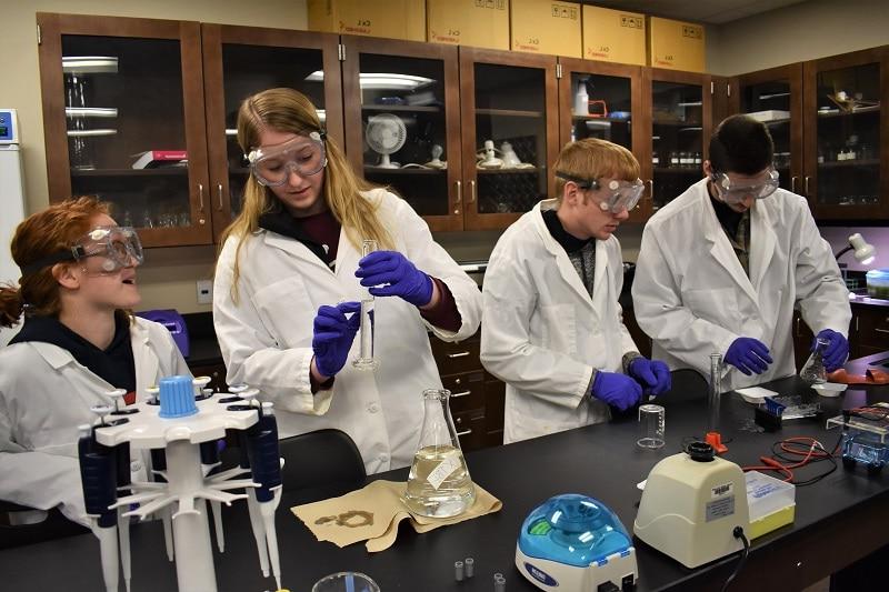 students in white lab coats conduct an experiment